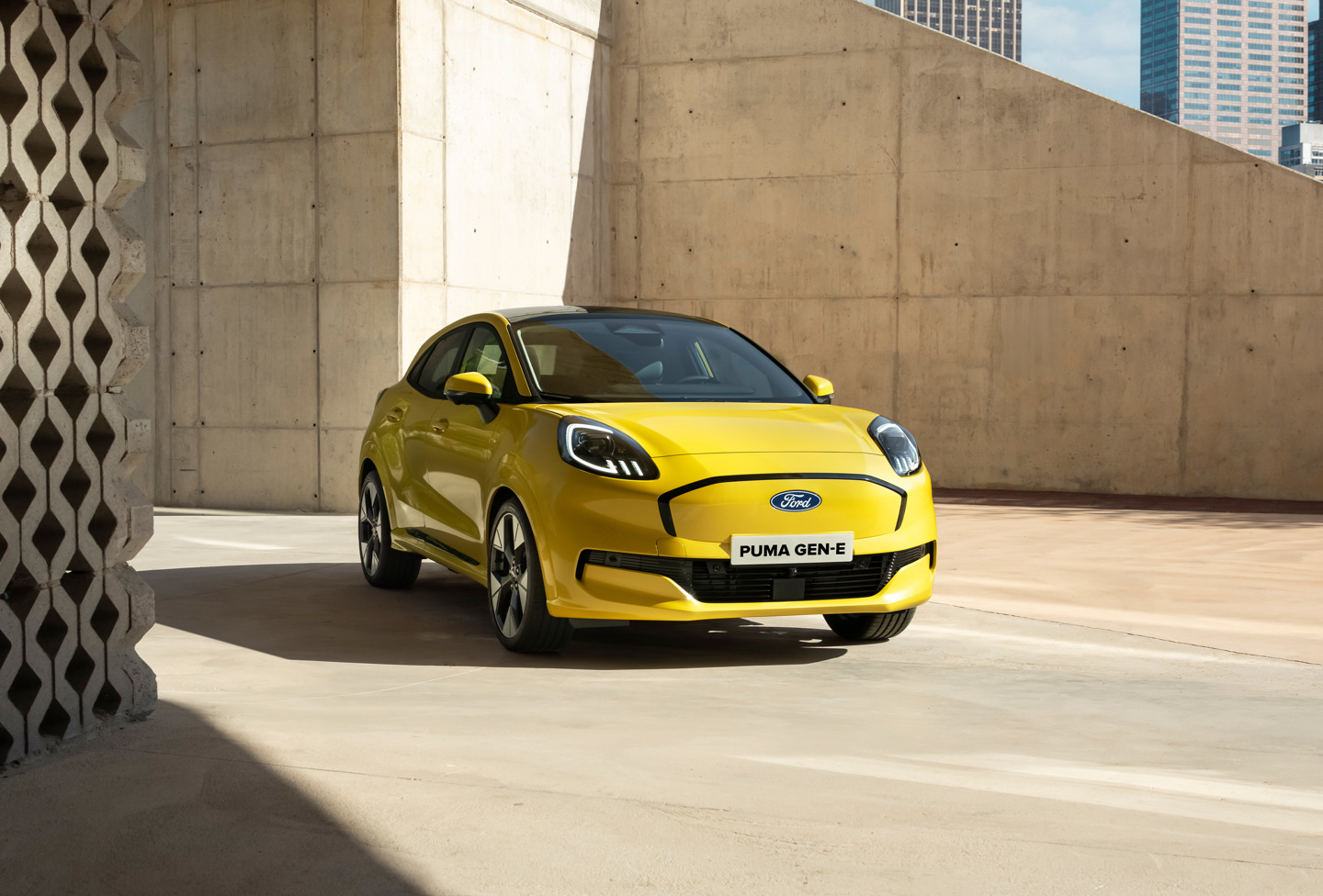 En gul Ford Puma Gen-E er parkeret stilfuldt i et moderne byområde, omgivet af slanke betonvægge og moderne bygninger i baggrunden.