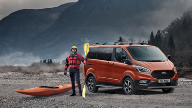 Orange Ford Tourneo Custom opbygning parkeret i bart landskab. Kajaksejler står ved siden af