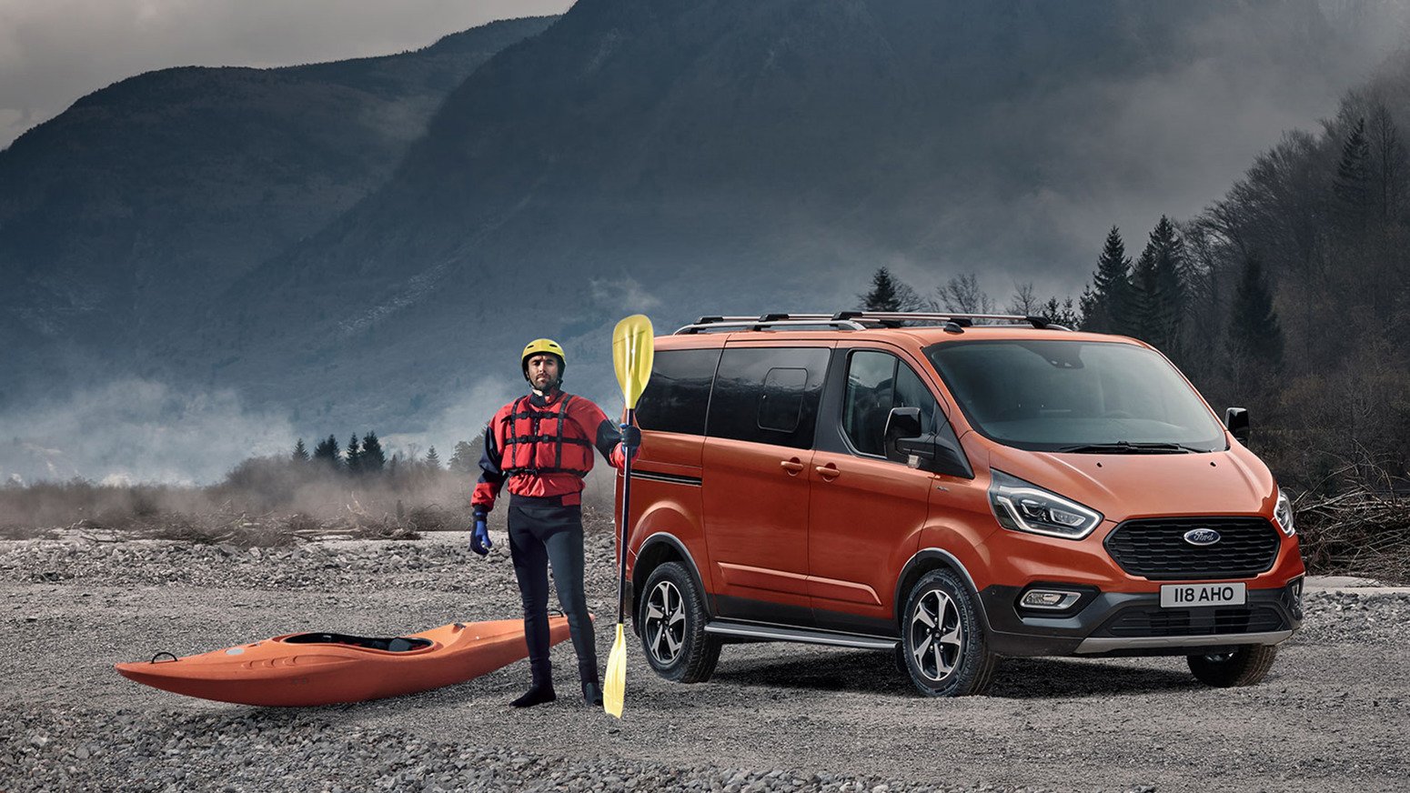 Orange Ford Tourneo Custom opbygning parkeret i bart landskab. Kajaksejler står ved siden af