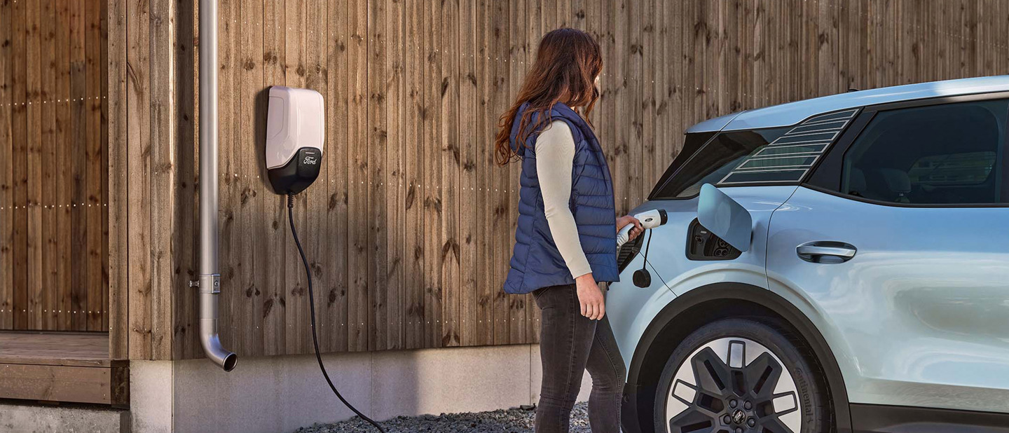Kvinde sætter Ford Explorer til at oplade ved Ford Connected Wallbox ved træhus 