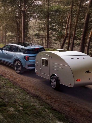 Et pixeleret billede af en bil, der trækker en lille trailer på en grusvej gennem et skovområde.