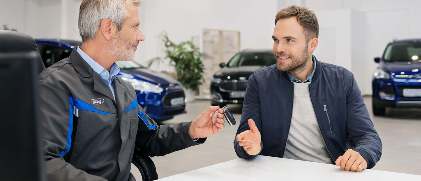 Ford medarbejder giver bilnøgle til mandlig kunde. Biler ses i baggrunden.