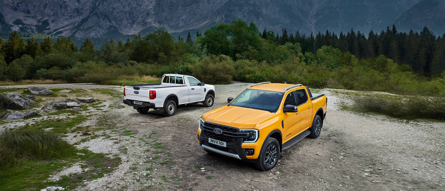 To Ford Ranger opbygninger parkeret i landskab omgivet af nåletræer.