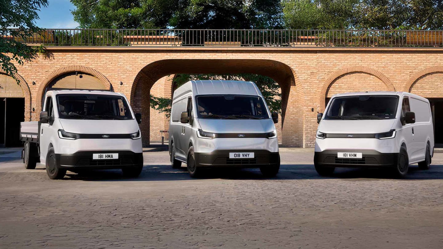 Tre hvide Ford el-varebiler er parkeret side om side foran en murstensbygning med buegange.