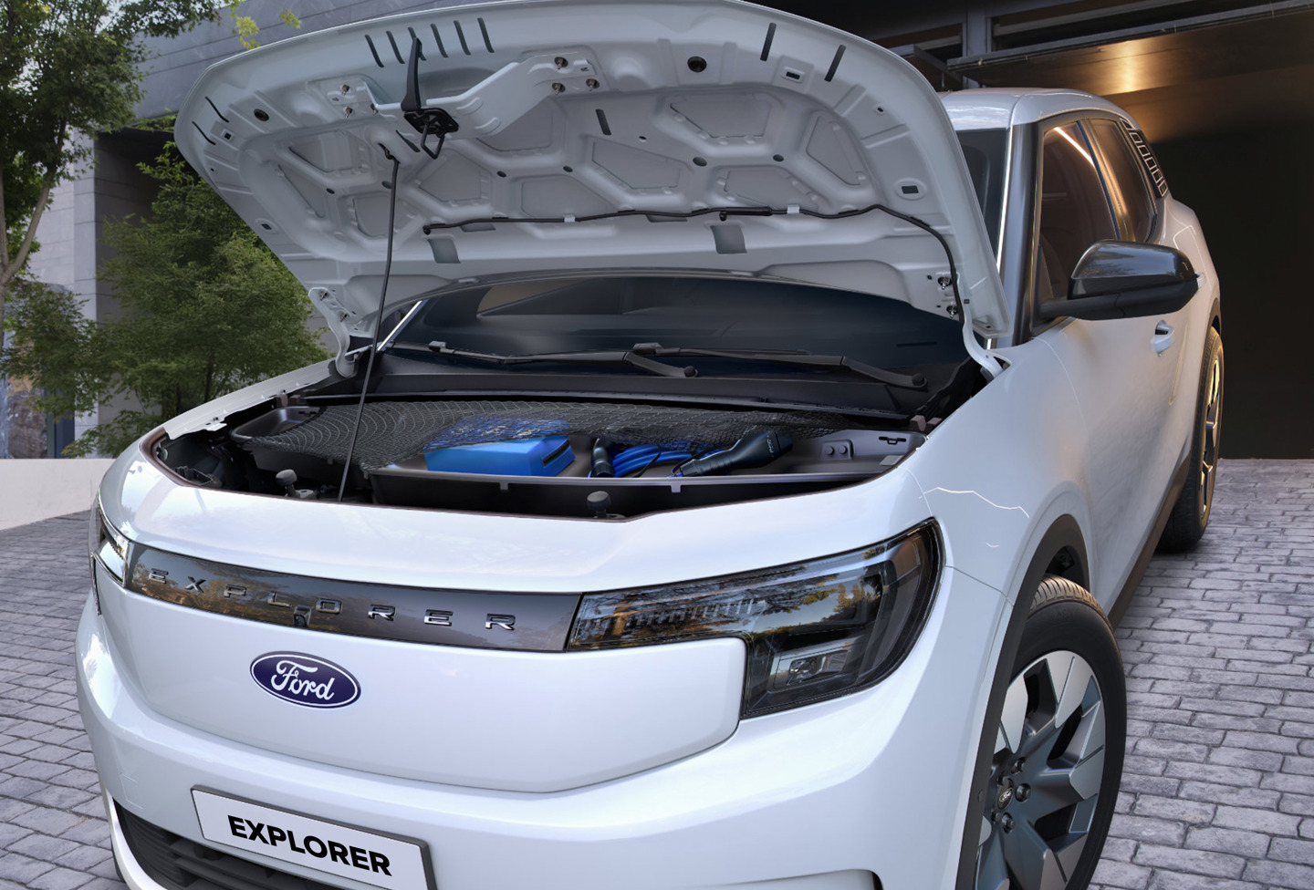 En hvid Ford Explorer med åben motorhjelm, der viser motorrummet, parkeret i en asfalteret indkørsel.