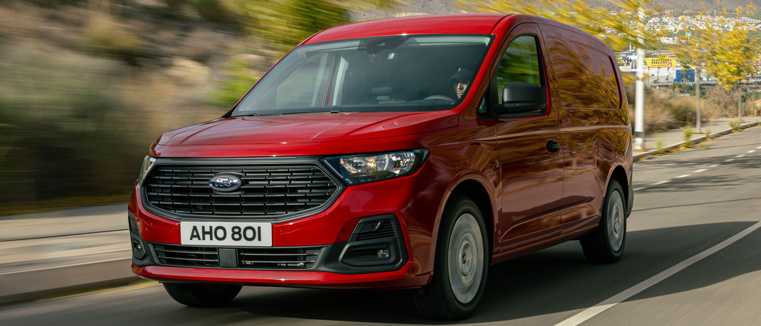 Rød Ford Transit Connect kørende på vej set skråt forfra