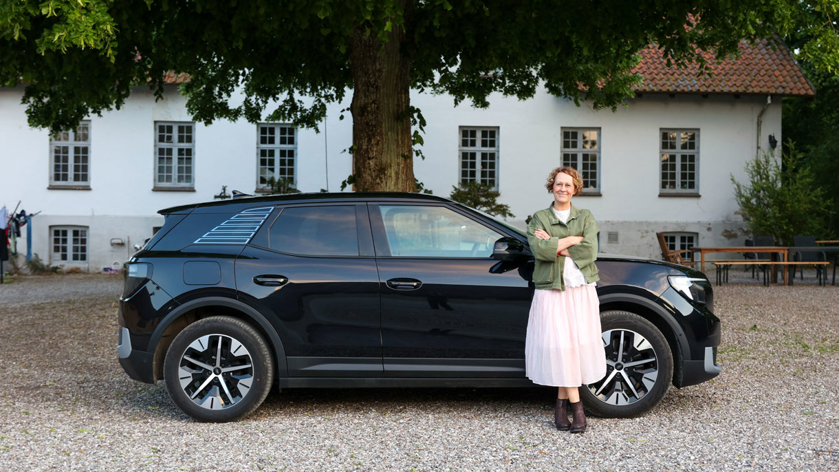 Rikke læner sig op af Ford Explorer parkeret foran sit hus